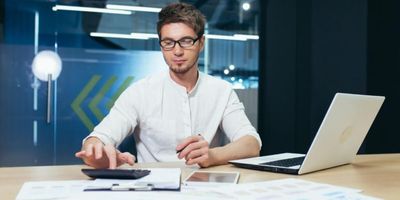 CFO de uma startup realiza cálculo em calculadora com laptop aberto